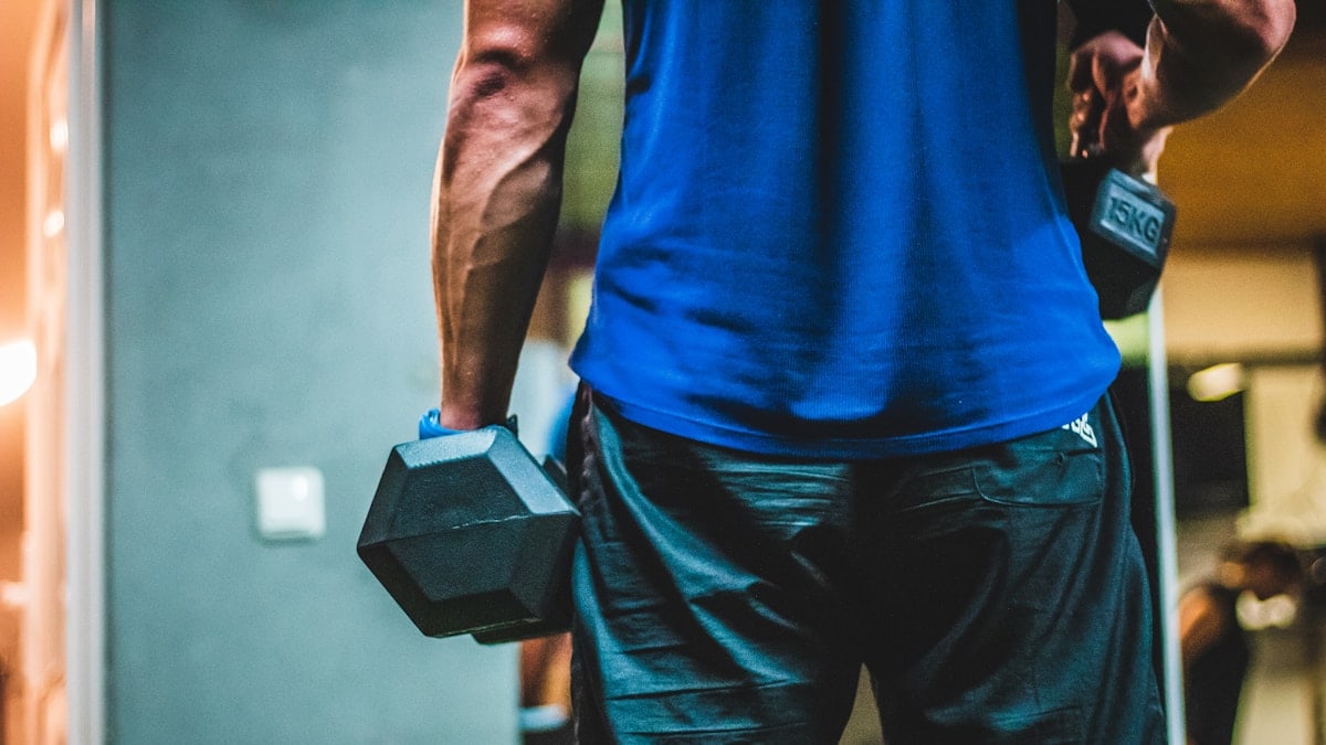 man in blue shirt carrying black dumbbells
